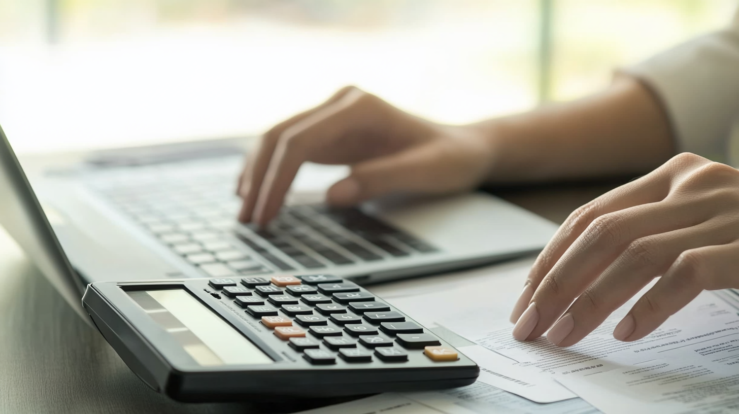 Ev sahibi ofis ortamında, mali belgeler ve hesap makinesiyle aylık giderleri hesaplayan kişi, bütçeleme ve maliyet analizi yapıyor.