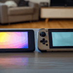 Ahşap masada yan yana duran, biri OLED ekranlı diğeri klasik LCD ekranlı iki taşınabilir oyun konsolu, doğal ışıkta.